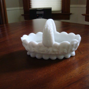 May include: White milk glass basket with a scalloped edge and a handle. The basket has a floral design.