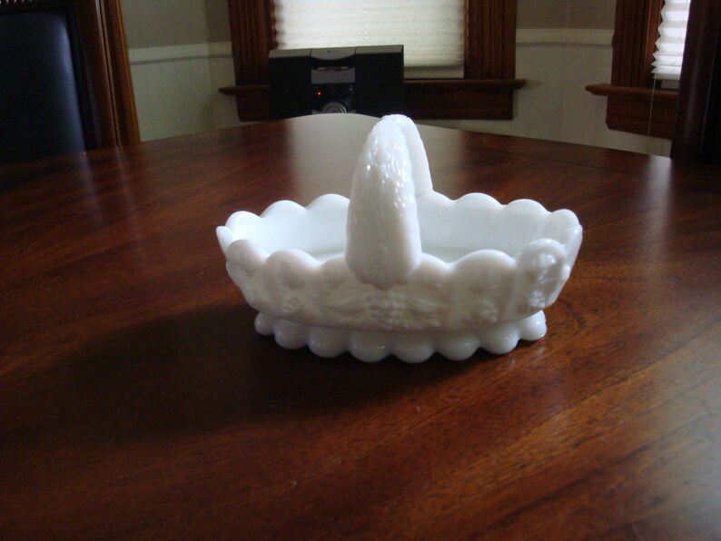 May include: White milk glass basket with a scalloped edge and a handle. The basket has a floral design.