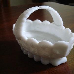 May include: White milk glass basket with a scalloped edge and a handle. The basket has a floral design.