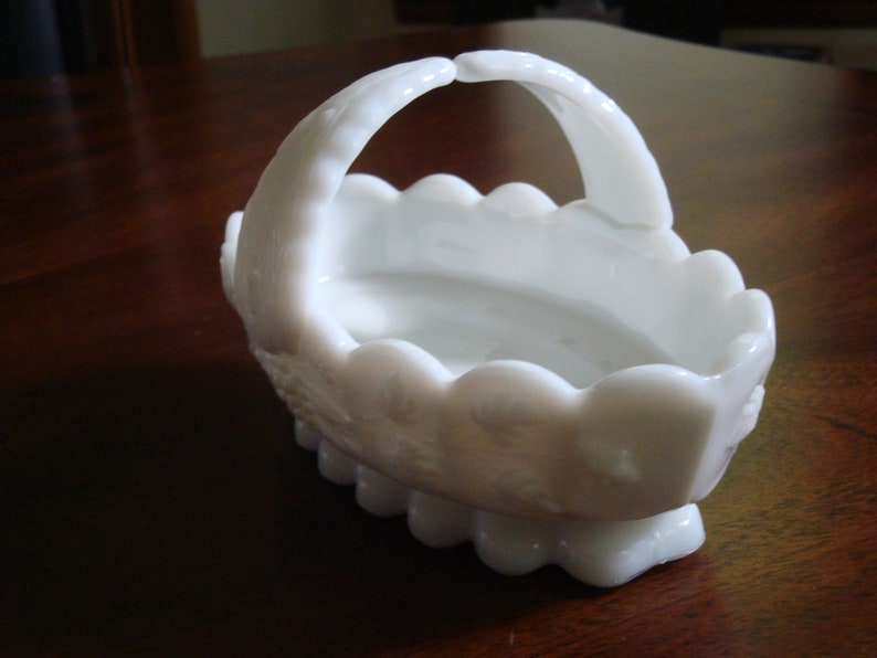 May include: White milk glass basket with a scalloped edge and a handle. The basket has a floral design.