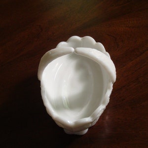 May include: White milk glass candy dish with a scalloped rim and a handle on each side. The dish is empty.
