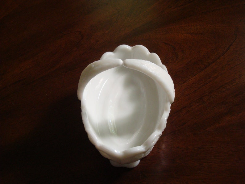 May include: White milk glass candy dish with a scalloped rim and a handle on each side. The dish is empty.