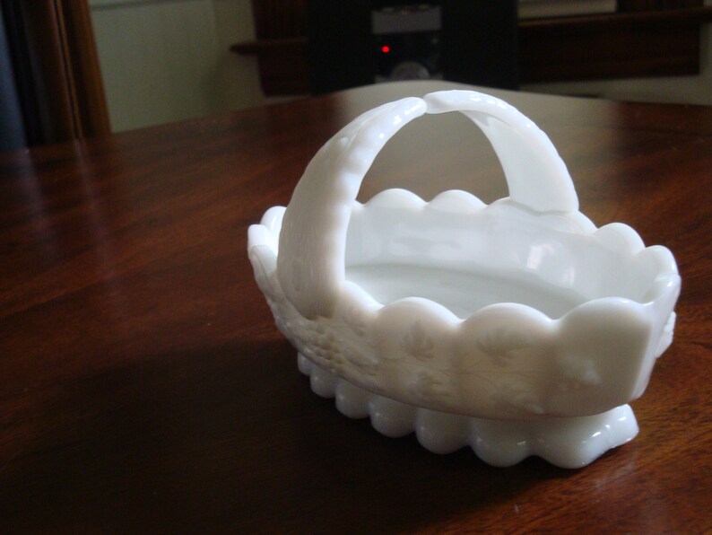 May include: White milk glass basket with a scalloped edge and a handle. The basket is decorated with a floral pattern.