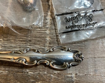 May include: Two silver spoons in plastic packaging with the text "Reed & Barton, Splendor" on the packaging.