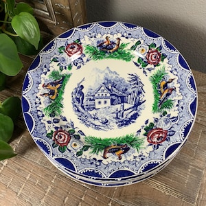 May include: Set of three blue and white ceramic plates with a scalloped edge. The plates feature a cottage scene with birds and flowers.