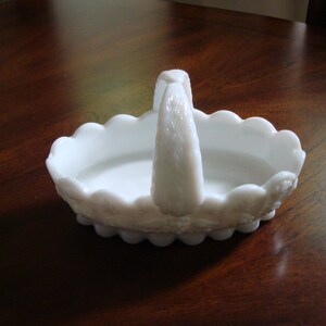 May include: White milk glass basket with a scalloped edge and a handle. The basket has a floral design.
