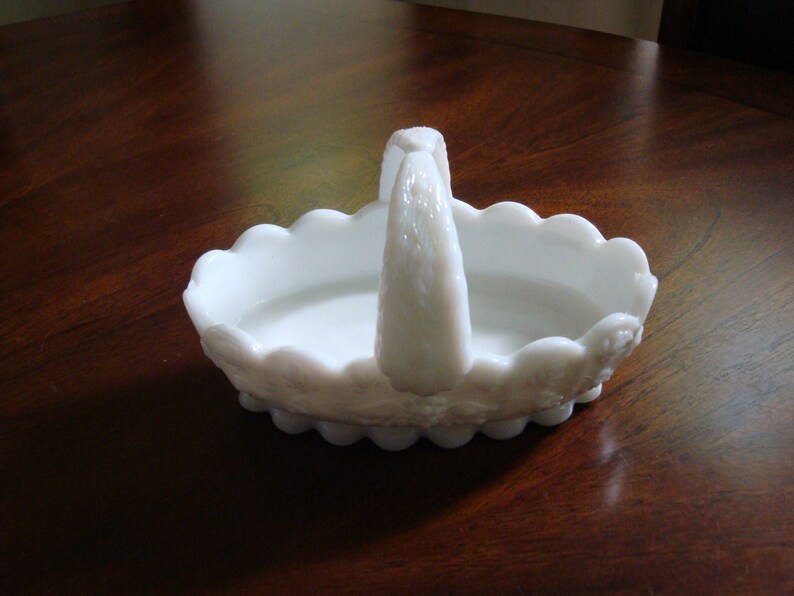 May include: White milk glass basket with a scalloped edge and a handle. The basket has a floral design.