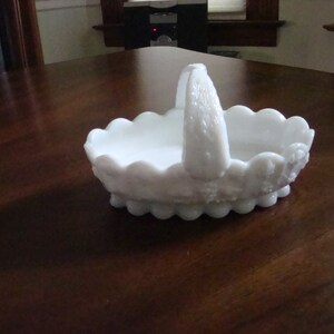 May include: White milk glass basket with a scalloped edge and a handle. The basket has a floral design.