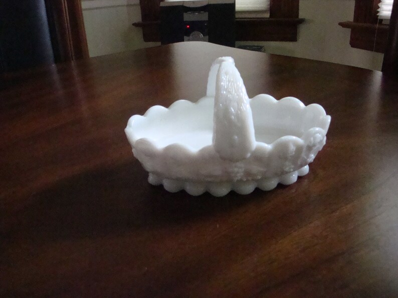 May include: White milk glass basket with a scalloped edge and a handle. The basket has a floral design.