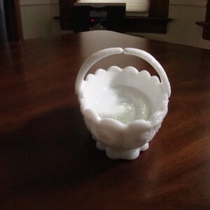 May include: White milk glass candy dish with a scalloped edge and a handle. The dish has a floral design.