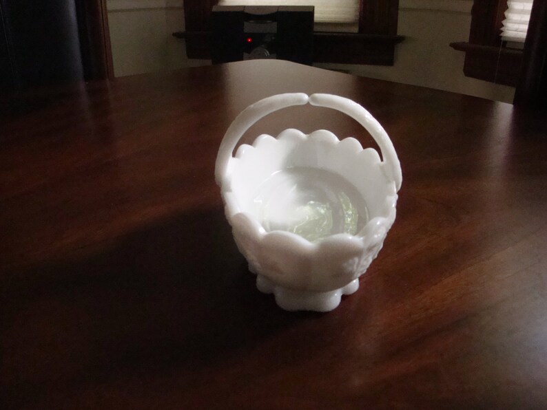 May include: White milk glass candy dish with a scalloped edge and a handle. The dish has a floral design.