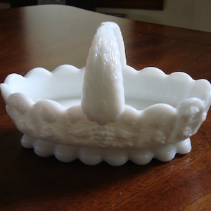 May include: White milk glass basket with a scalloped edge and a handle. The basket has a raised floral design.