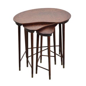 May include: A set of three nesting tables with a kidney bean shape. The tables have dark brown wooden legs with brass tips and matching oval tops. The largest table is approximately 30 inches long.