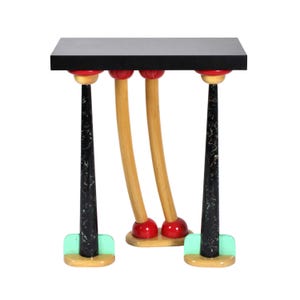May include: A whimsical side table with a black rectangular top. The table has three curved, light-brown legs with red ball feet and black, marble-patterned supports. The base of the legs are light green. The table is a unique piece of furniture.