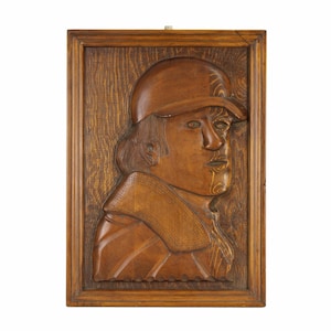 May include: A wooden relief sculpture of a person's head and shoulders wearing a hat. The sculpture is framed in a dark wood frame.