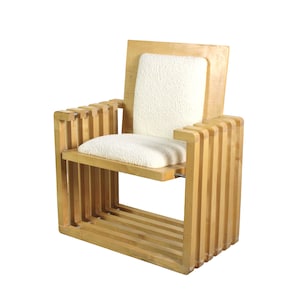 May include: A light-colored wooden armchair with a rectangular back and armrests. The chair features a seat and back cushion made of a white, textured fabric. The design incorporates vertical wooden slats for the armrests and base.