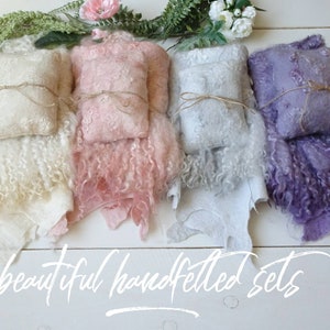 May include: Three sets of hand-felted baby wraps and pillows. The sets are in cream, pink, and purple. Each set includes a small pillow and a larger wrap.