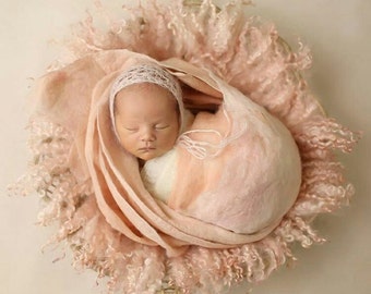 May include: A newborn baby is sleeping peacefully in a pink basket, wrapped in a soft, pink and white blanket. The baby is wearing a white crocheted hat.