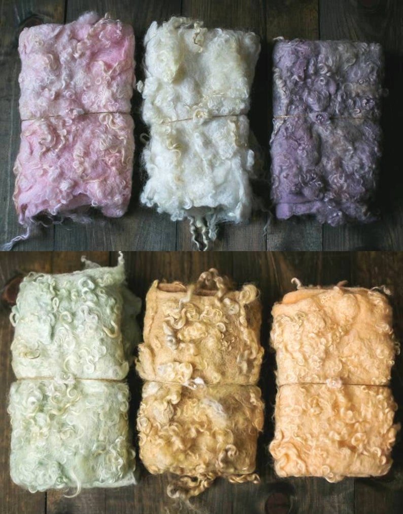 May include: Six different colors of curly sheep wool, each rolled up and tied with twine. The colors are pink, white, purple, green, yellow, and orange.