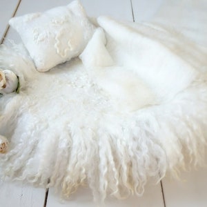 May include: White fluffy newborn photography prop with a white pillow and white flowers.