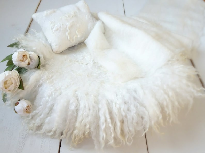 May include: White fluffy newborn photography prop with a white pillow and white flowers.