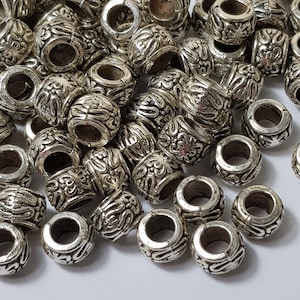 May include: A pile of silver metal beads with an ornate design. The beads are round and have a hole in the centre. They are perfect for jewellery making or other crafts.