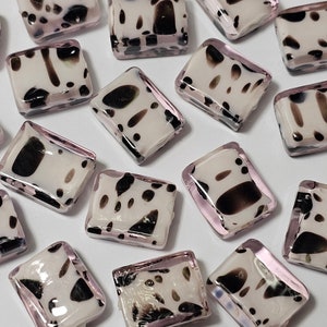 May include: A collection of small, rectangular glass tiles with a white background and black abstract patterns. The tiles have a pink border and are perfect for crafting projects.