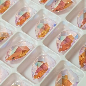 May include: A close-up of a white tray filled with iridescent teardrop-shaped crystals. The crystals have a pink and orange hue and are arranged in rows.