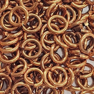 Op de afbeelding: Close-up van een stapel koperkleurige sprongringen. De ringen zijn ovaal van vorm en hebben een heldere, metallic afwerking. Ze zijn dicht op elkaar gepakt, waardoor een textuur ontstaat. Ideaal voor het maken van sieraden en knutselen.