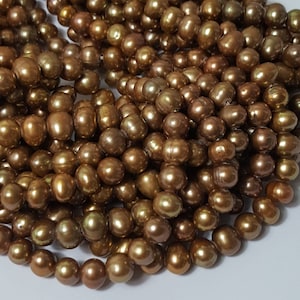 Peut inclure: Gros plan sur un tas de perles brillantes, brun doré. Les perles ont une forme ovale irrégulière et une surface lisse et réfléchissante. La couleur varie légèrement, créant de la profondeur et de l'intérêt visuel. Les perles sont enfilées, suggérant qu'elles sont prêtes pour la bijouterie.