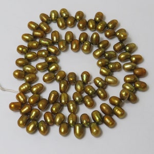 Pode incluir: Um fio de pérolas douradas iridescentes, dispostas em um padrão circular. As pérolas são de forma oval e têm um acabamento liso e brilhante.