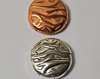 May include: Two round metal beads with a wavy pattern. One bead is copper and the other is silver.