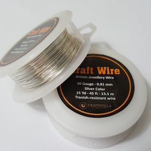 Può includere: Un rotolo di filo artigianale argentato in un contenitore di plastica trasparente. L'etichetta riporta "Craft Wire", "Artistic Jewellery Wire", "20 Gauge - 0.81 mm", "Silver Color", "15 Yd - 45 ft - 13.5 m", "Tranish-resistant wire", e "CRAFTSVILLA".
