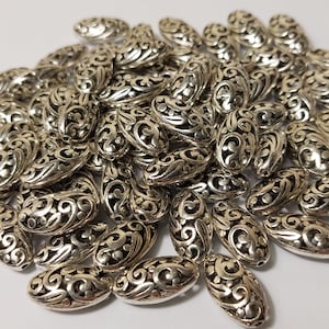 May include: A pile of silver oval-shaped beads with a decorative filigree design.