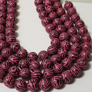 May include: A strand of pink and black zebra print beads. The beads are round and have a glossy finish.