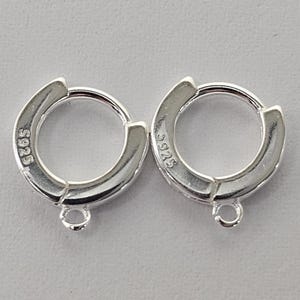 May include: A pair of silver hoop earrings. Each earring features a hinged clasp and a small loop at the base. The hallmark "S925" is visible on each earring. These earrings are designed for pierced ears.