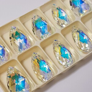 May include: A set of ten iridescent teardrop-shaped crystal pendants in a white plastic storage box. The crystals are clear with a rainbow effect.