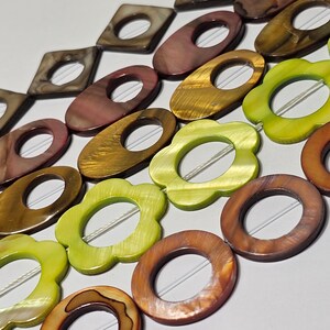 May include: A strand of colourful shell beads in various shapes and sizes. The beads are brown, green, and gold with a pearlescent finish. Each bead has a hole in the centre for stringing.