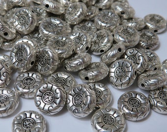 May include: A large pile of silver metal beads with a decorative design. The beads are oval shaped and have a raised design.