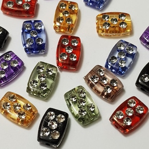 May include: Assortment of colorful rectangular beads with rhinestones. The beads are made of glass and have a variety of colors, including red, blue, green, purple, and black.