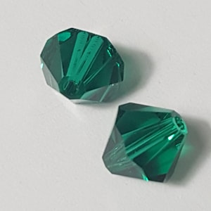Può includere: Due perline di vetro sfaccettate di colore verde smeraldo con un foro al centro per l'infilaggio.