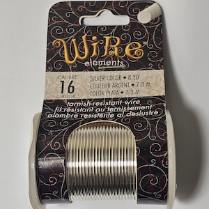 May include: A spool of silver-coloured, tarnish-resistant wire. The label reads "Wire elements", "Calibre 16 Gauge", "Silver Color 8 YD", "Couleur Argent 7.3 M", "Color Plata 7.3 M", "tarnish-resistant wire", "fil résistant au ternissement", "alambre resistente al deslustre".