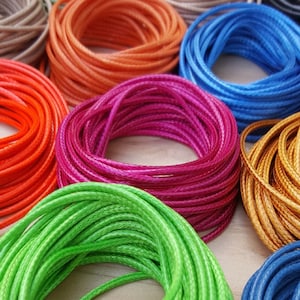 May include: Assortment of colourful cords in various shades of orange, blue, green, pink, gold, and brown. The cords are wound into coils and are likely used for crafting or jewellery making.