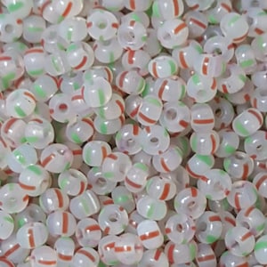 May include: A close-up of a pile of white seed beads with red and green stripes. The beads are small and round, and they are ideal for jewellery making.