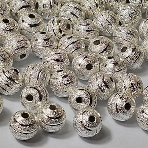 May include: A large pile of silver metal beads with a textured, grooved surface. The beads have a hole in the centre for stringing.