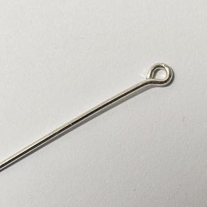 May include: A silver head pin with a loop at the end. The pin is straight and has a smooth finish.