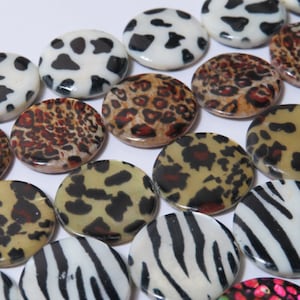 以下が含まれることがあります： 牛、ヒョウ、シマウマ、チーターなど、さまざまな動物柄のパターンが施された、丸くて平らな装飾用ビーズのセット。ビーズは白、黒、茶色、ベージュです。