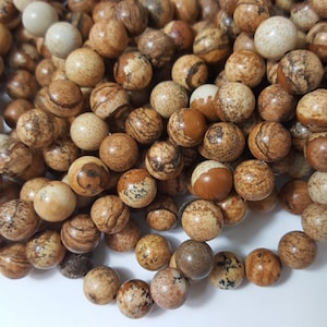 May include: A strand of brown and white patterned gemstone beads. The beads are round and have a smooth, polished finish.