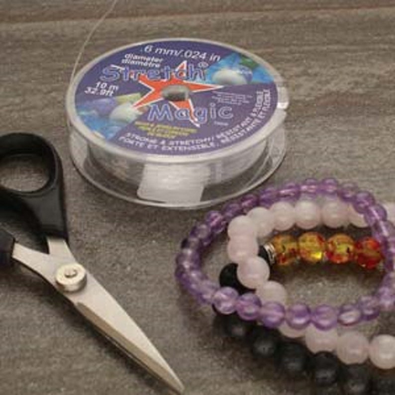 May include: A spool of clear elastic stretch magic thread for jewelry making. The spool is labeled "Stretch Magic" and has a 6 mm diameter. A pair of scissors and three bracelets made with the thread are also pictured.