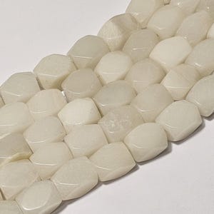 May include: Close-up of a strand of off-white, faceted gemstone beads. The beads have a smooth, polished surface and a slightly irregular shape. The beads are strung together, creating a continuous line of colour and texture. The overall effect is one of simple elegance.